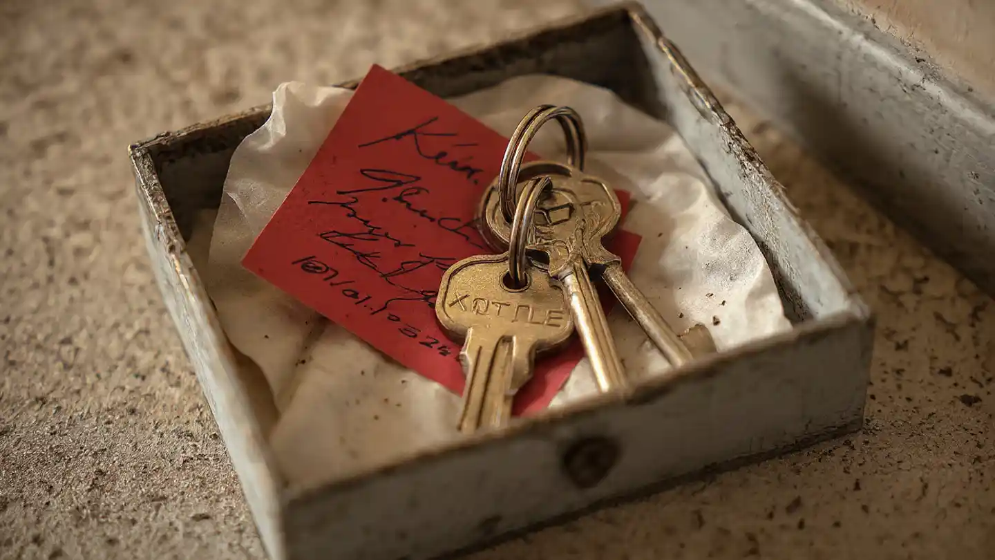 Close-up of house keys and a note in a small box lying on a laundry room floor.