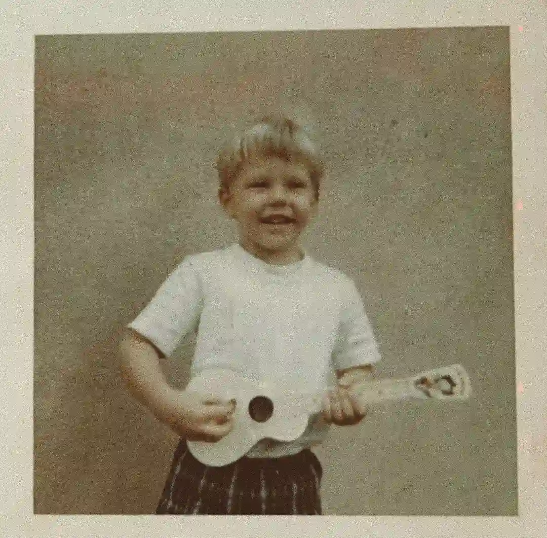A young boy practicing guitar in a small bedroom.