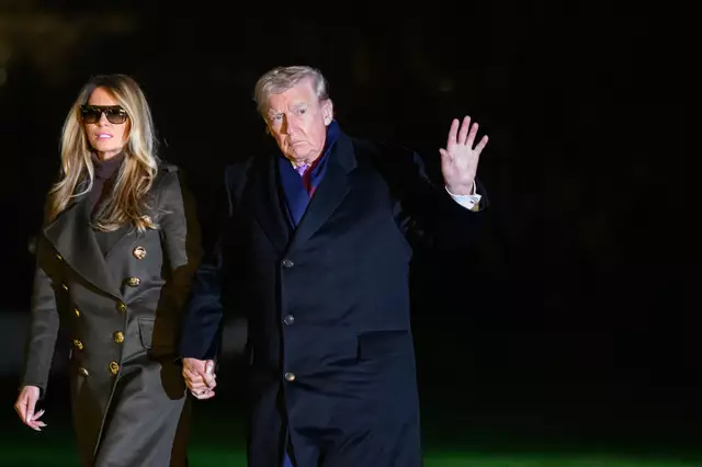 Donald Trump and Melania Trump holding hands and walking across a grassy area at night after departing Marine One. Melania is wearing a dark coat and large sunglasses.