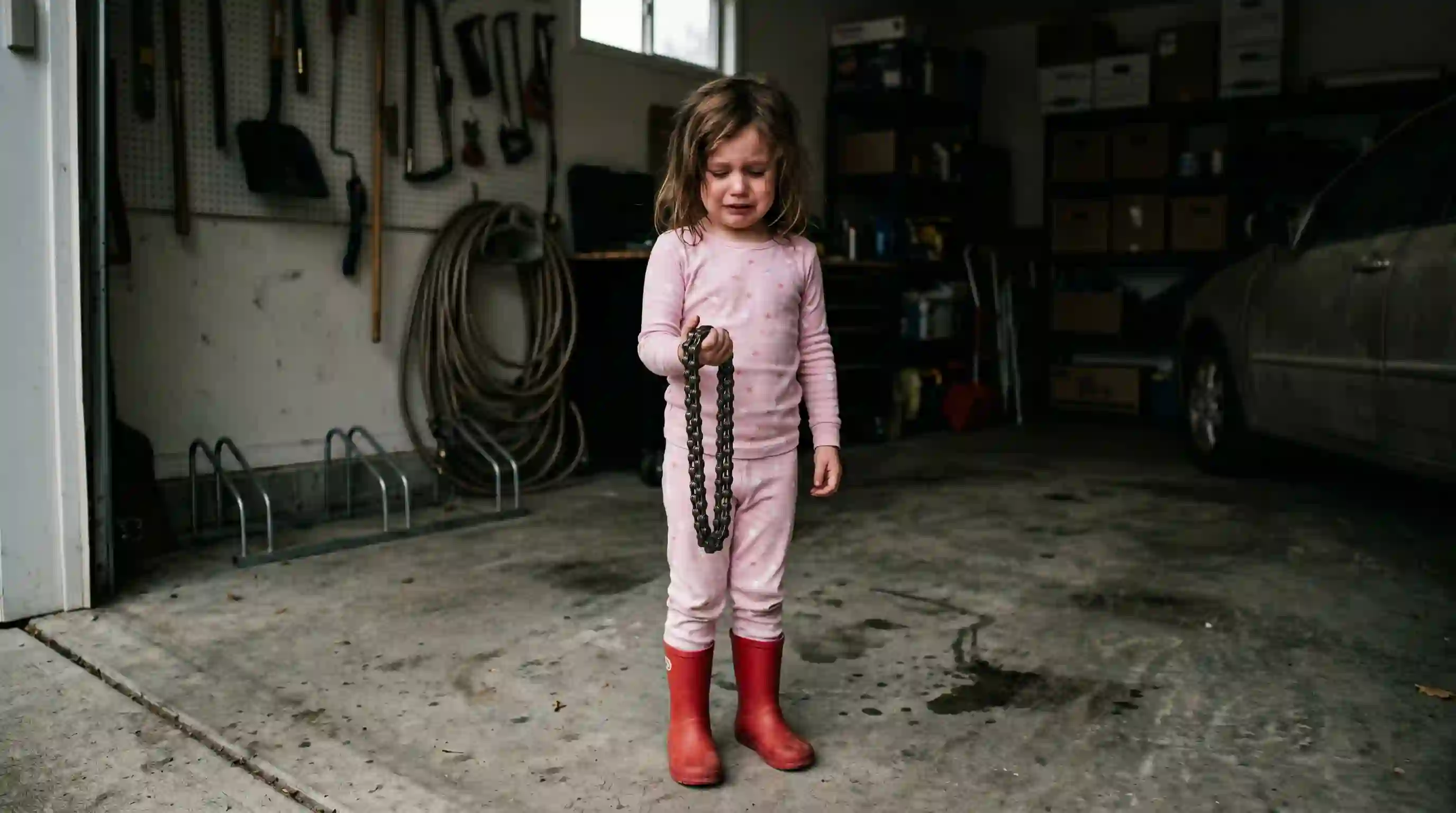Little girl crying in an empty garage holding a bike lock