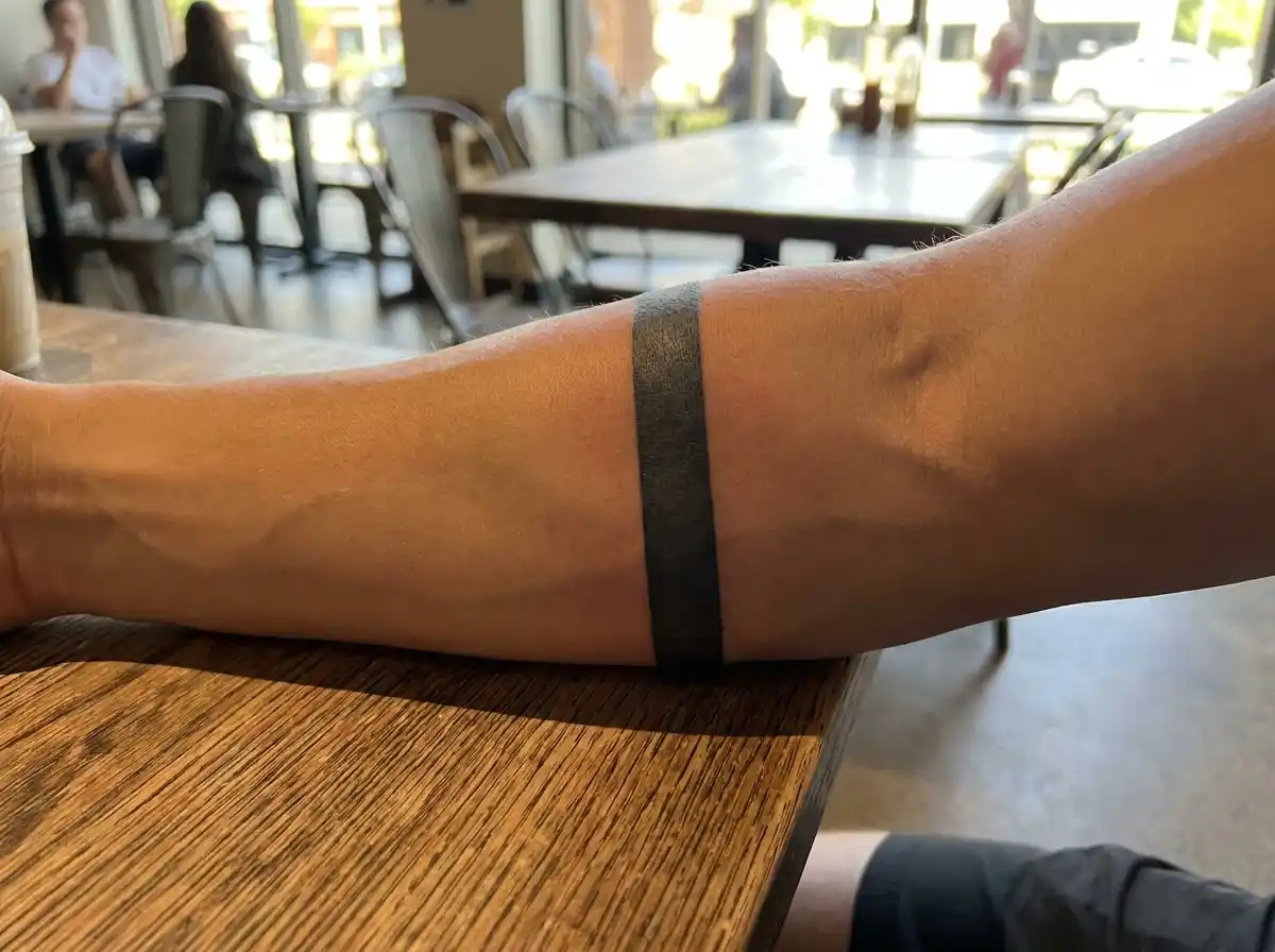 A sleek minimalist solid black band tattoo wrapped elegantly around a forearm