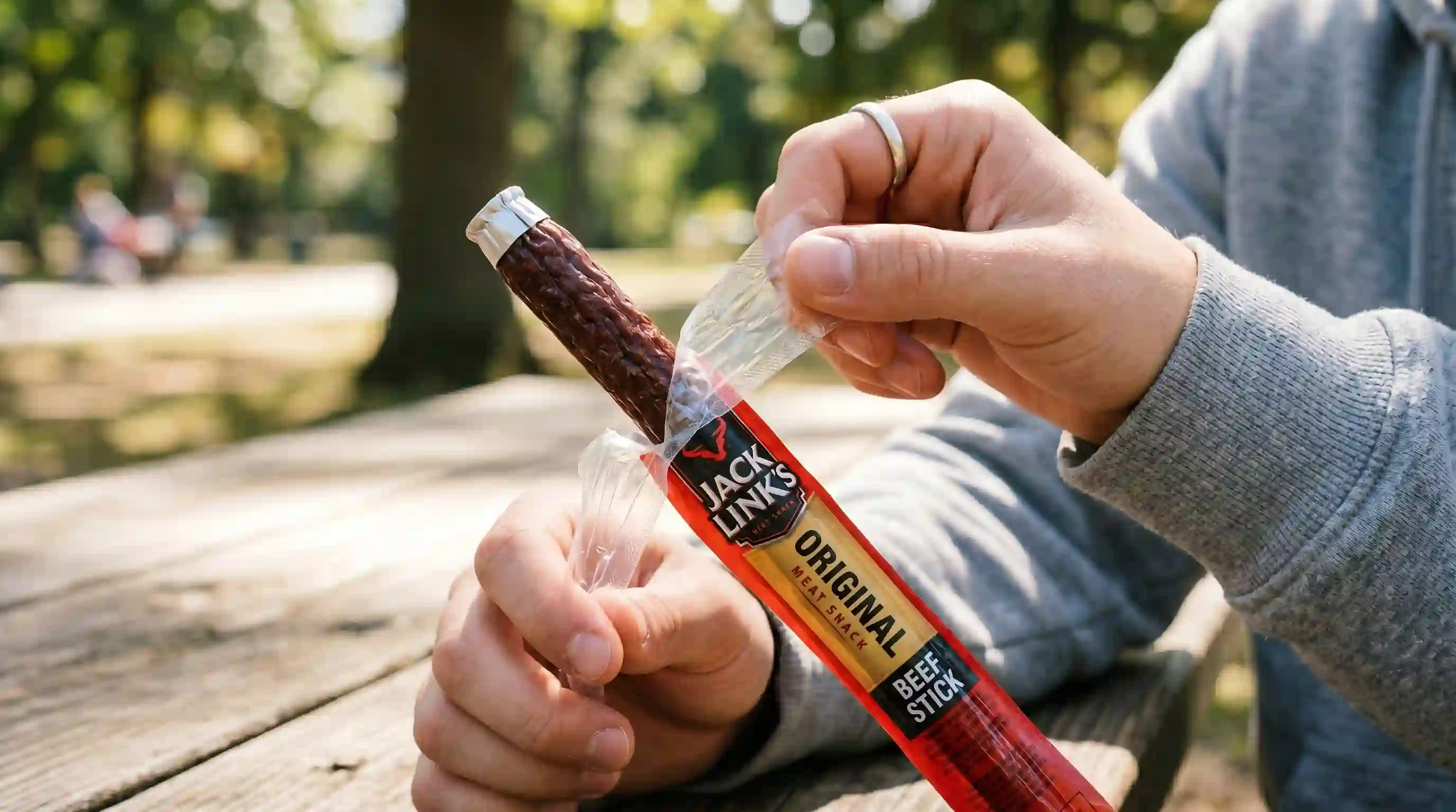 Hands opening a sausage snack stick, revealing the metal ring at the top