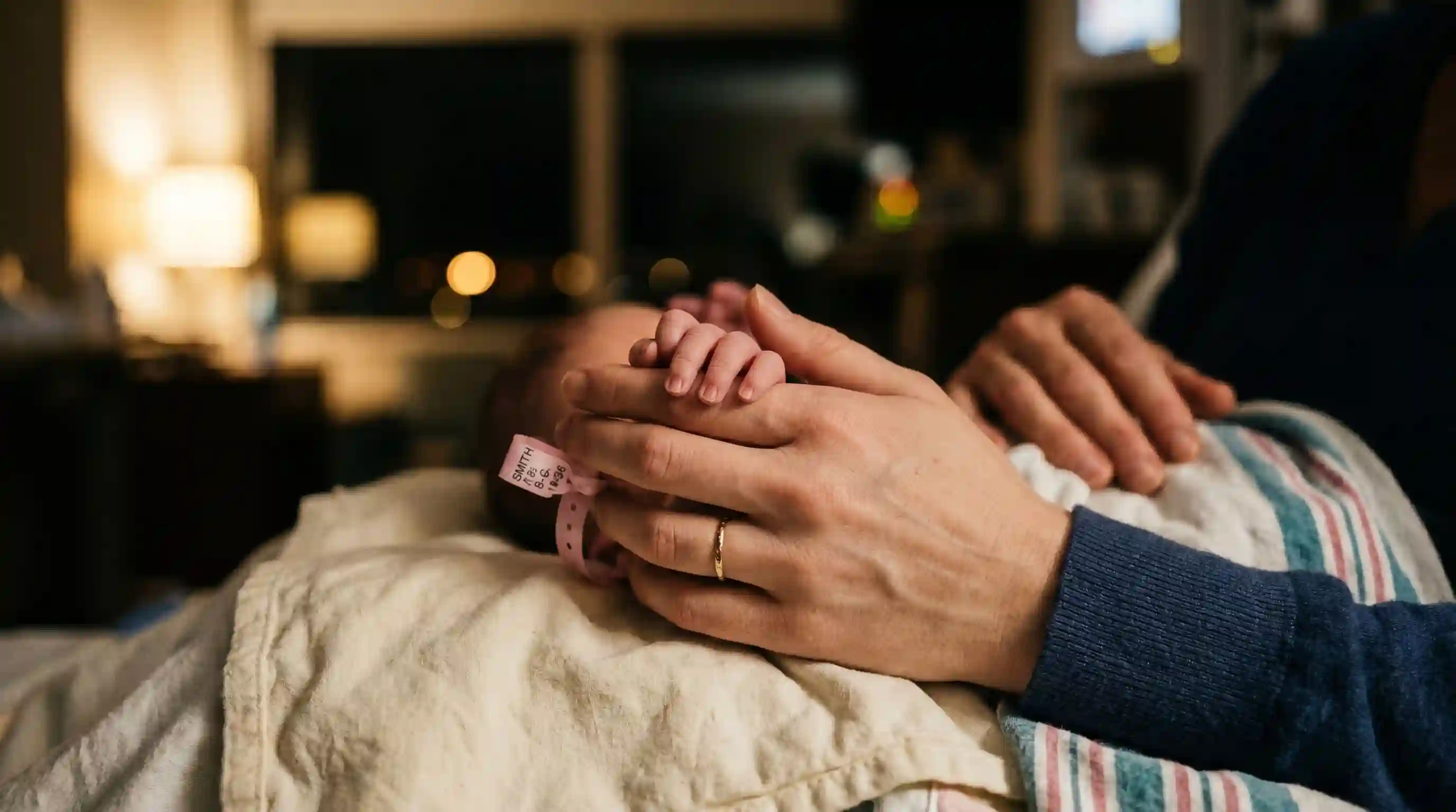 A woman's hand gently holding the tiny fingers of a newborn baby