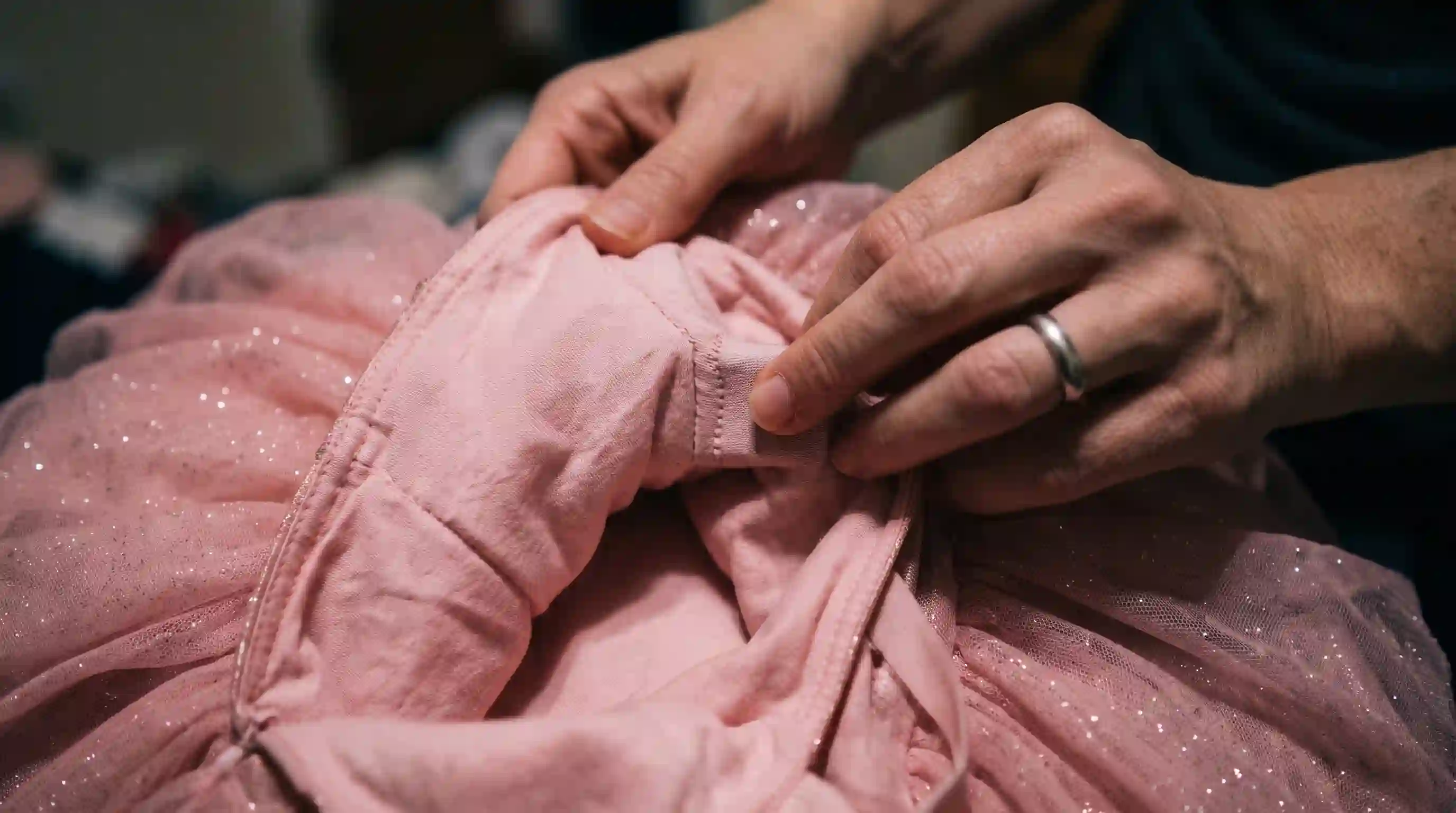 Close up of a mother's hands feeling a stiff bump hidden inside the lining of a pink dress