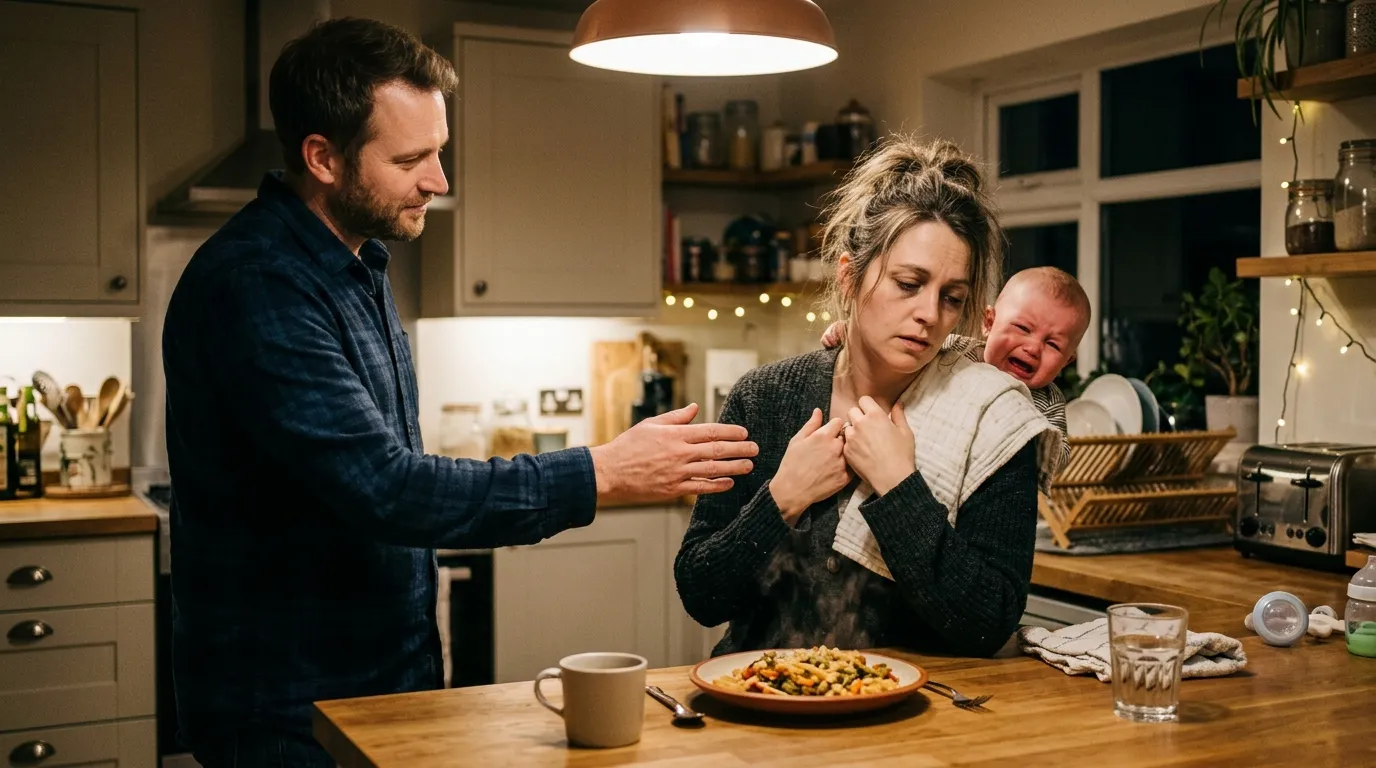 A caring friend taking a crying baby from an exhausted mother at the dinner table.