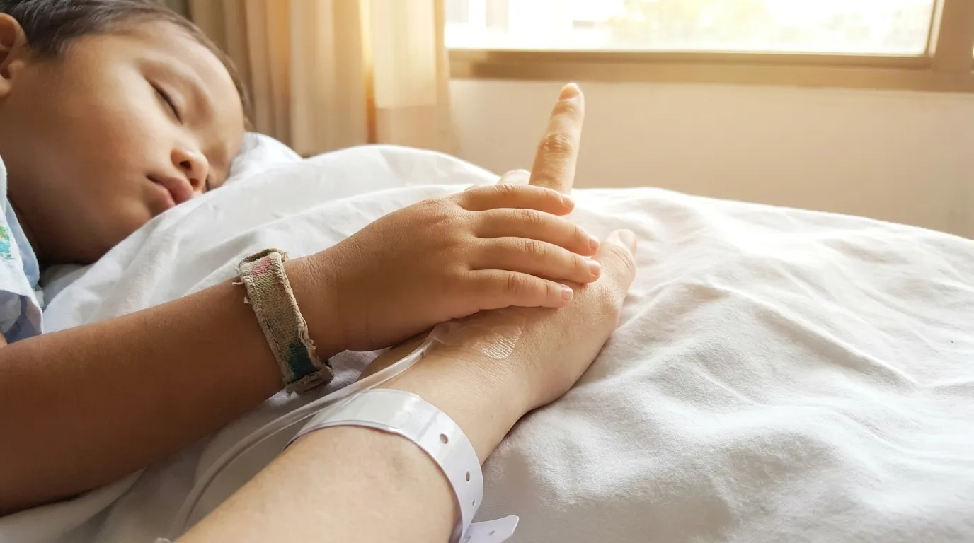 Close up of a child's hand holding a woman's hand on a hospital bed, with one finger slightly raised