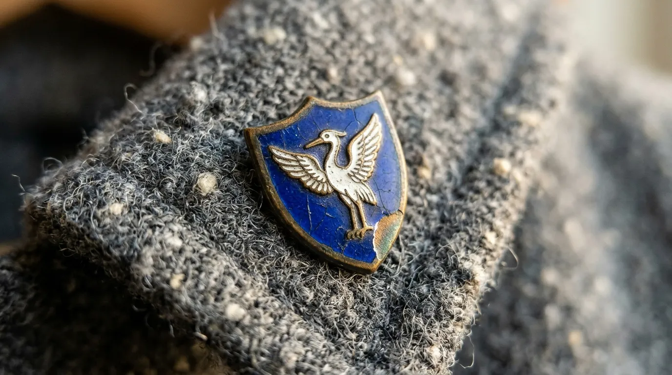 Close up of a vintage, chipped brass pin with a blue shield and white heron on a gray wool coat